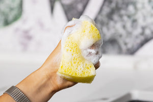 spugna gialla in mano con schiuma bianca