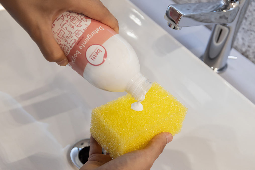 bottiglia di detergente bagno, bianco, versato su spugna gialla sopra un lavandino
