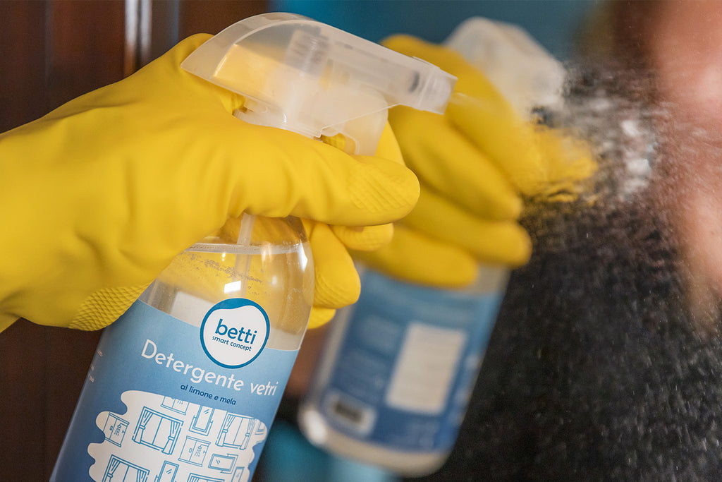 detergente vetro con spruzzino, prodotto sul vetro, mano con guanto giallo